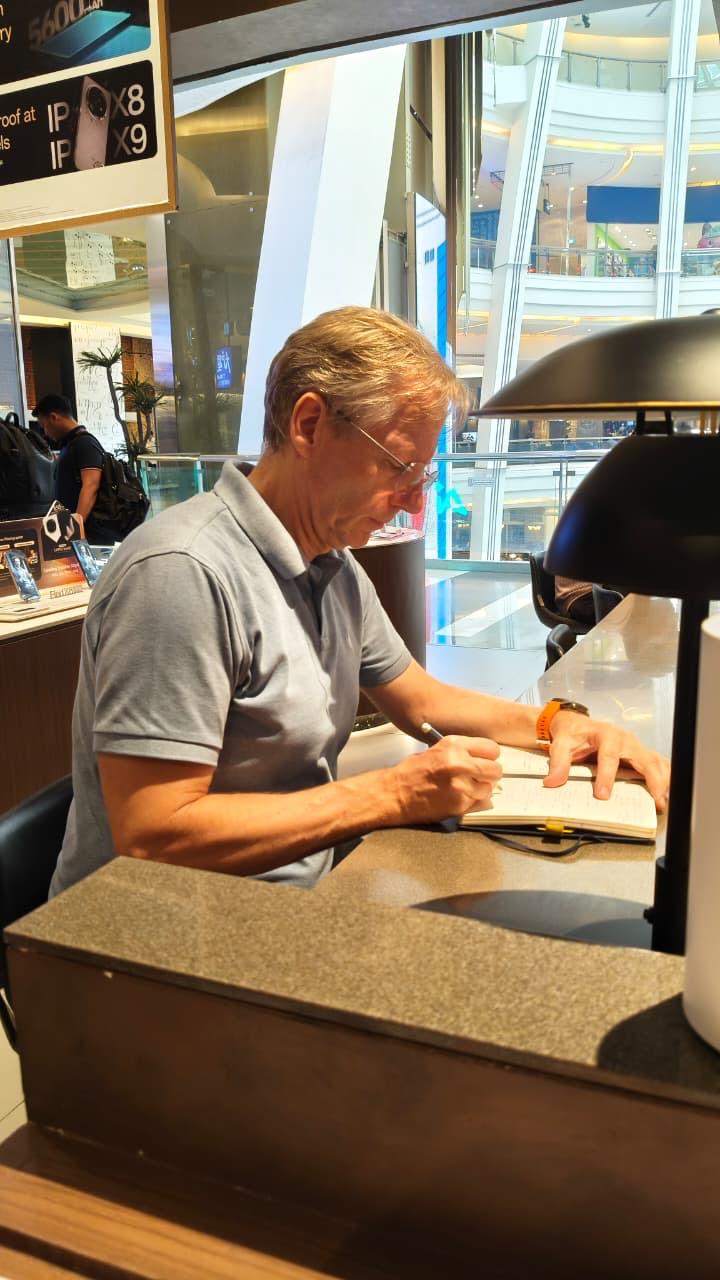Joerg sitting at a desk writing in his journal and reflecting. Cafe, Mall setting.