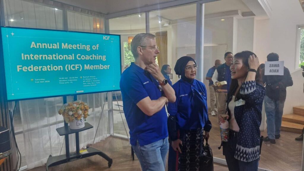 Joerg at ICF Jakarta Charter Chapter annual event in discussion with a few leadership members. A TV screen with the meeting title in the background. A group of people in the back.